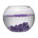 A clear bowl filled with water with purple magic sand in the bottom