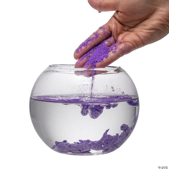 A clear bowl filled with water with purple magic sand in the bottom.  A hand is shown coming out of the bowl with Magic sand showing the hydrophobic properties.